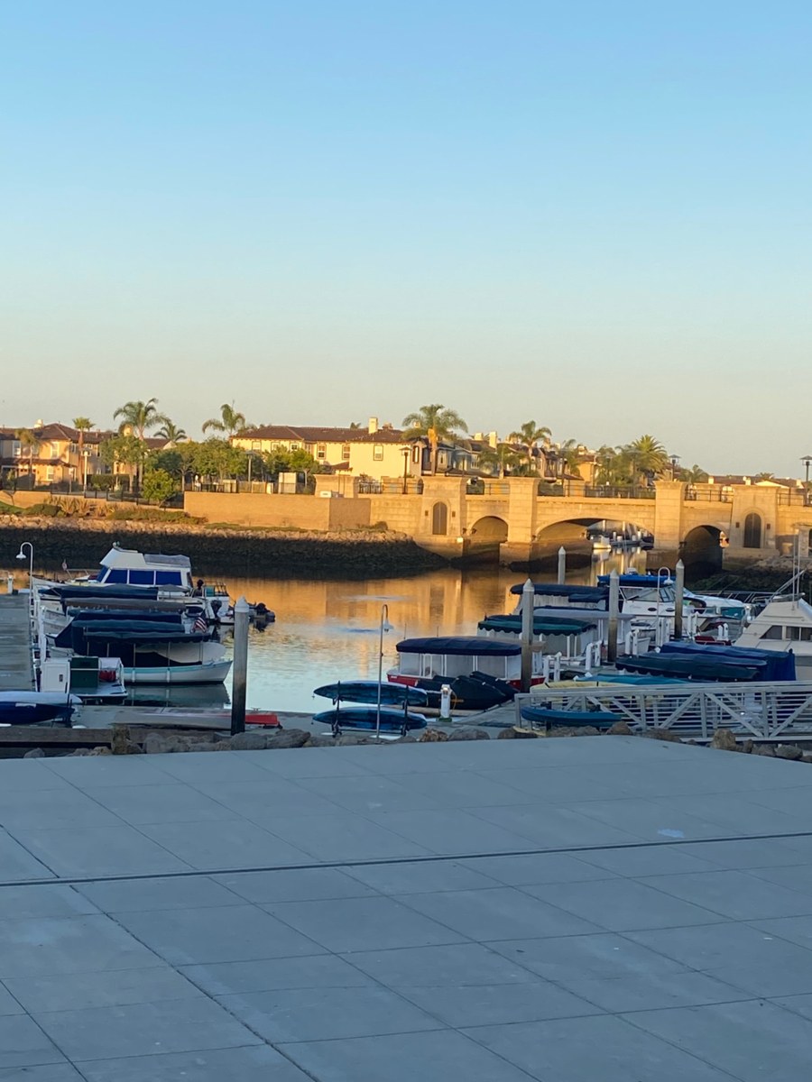 A stone harbor bridge in warm golden light, overlooking moored boats and calm water.
